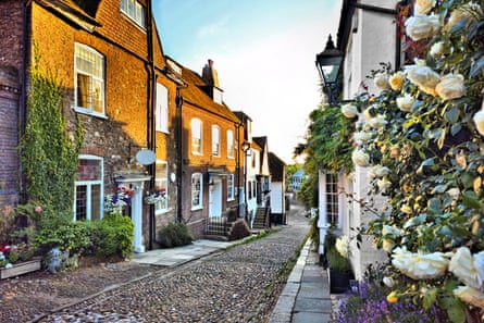 A sunlit cobblestone sloping street with old terraced houses adorned with flowers