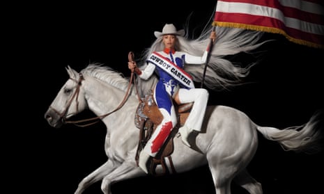 woman holding us flag and riding white horse. she wears red, white and blue, a sash that says 'cowboy carter', and a cowboy hat