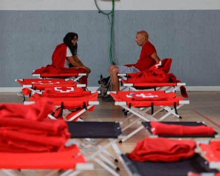 two people sitting on camp beds with empty beds in front of them