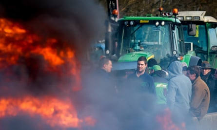 Flames are seen in the foreground as farmers with tractors block a highway