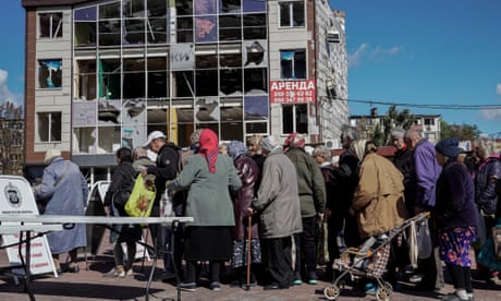 People queue for food distribution beside a damaged building in Mariupol, eastern Ukraine