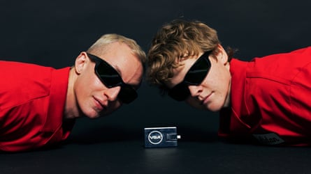 two people in red shirts and black sunglasses look to side as they lean over USB drive
