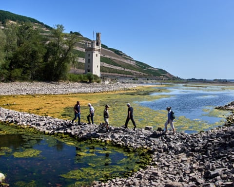 People walk over a stone dam across a low river