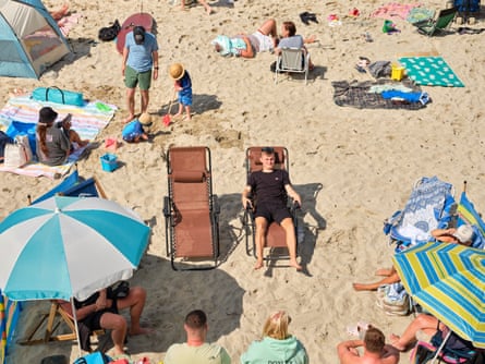 People on deckchairs and under sun umbrellas on a beach in St Ives, Cornwall, UK, July 2024