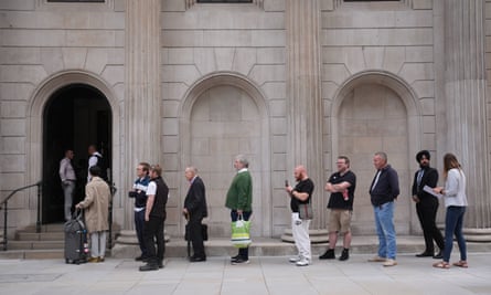 People form a line with a light stone-coloured building behind them