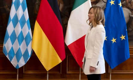Giorgia Meloni standing in front of a row of flags. 