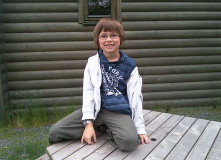 A young Tom Parfett smiles at the camera sitting on a garden table