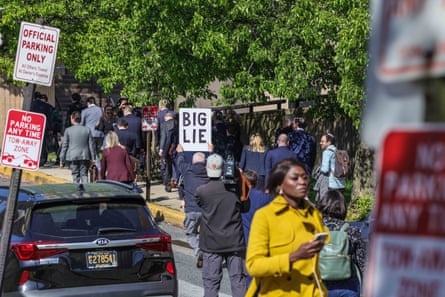 A group of people in suits walk down a street followed by a man holding a sign that reads ‘Big lie’.