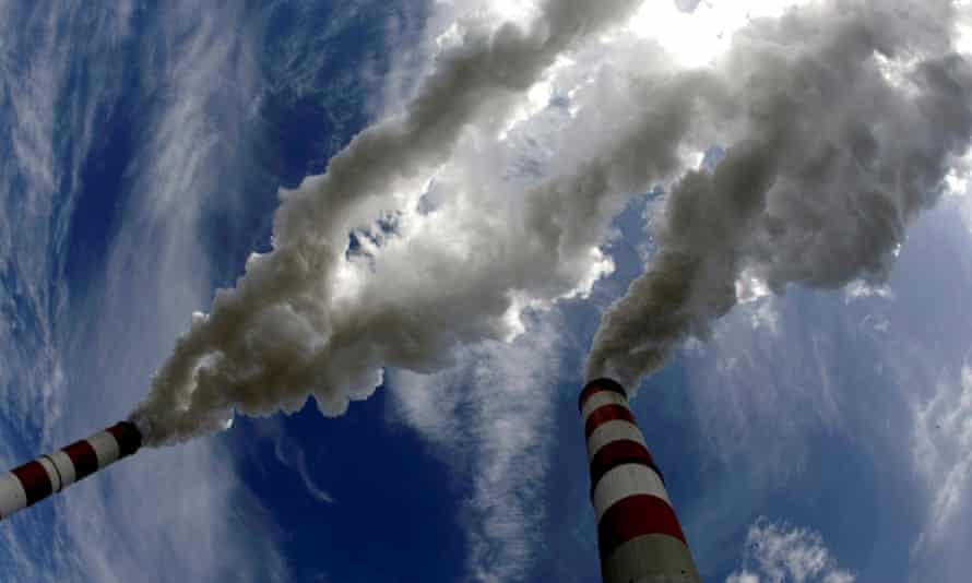 Two power station chimneys shot from directly below, emitting plumes of smoke against a background of blue sky