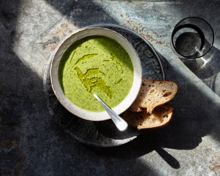 Overhead view of thick watercress soup in a bowl with two slices of bread on a plate and a cup of water