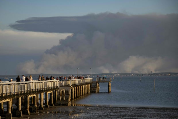 Tourists look at the plume of dark smoke on the shoreline of Arcachon from the pier in Andernos-les-Bains, due to a wildfire in a forest near La Teste , southwestern France, 14 July