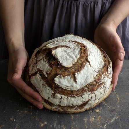 A baker holding a round sourdough loaf