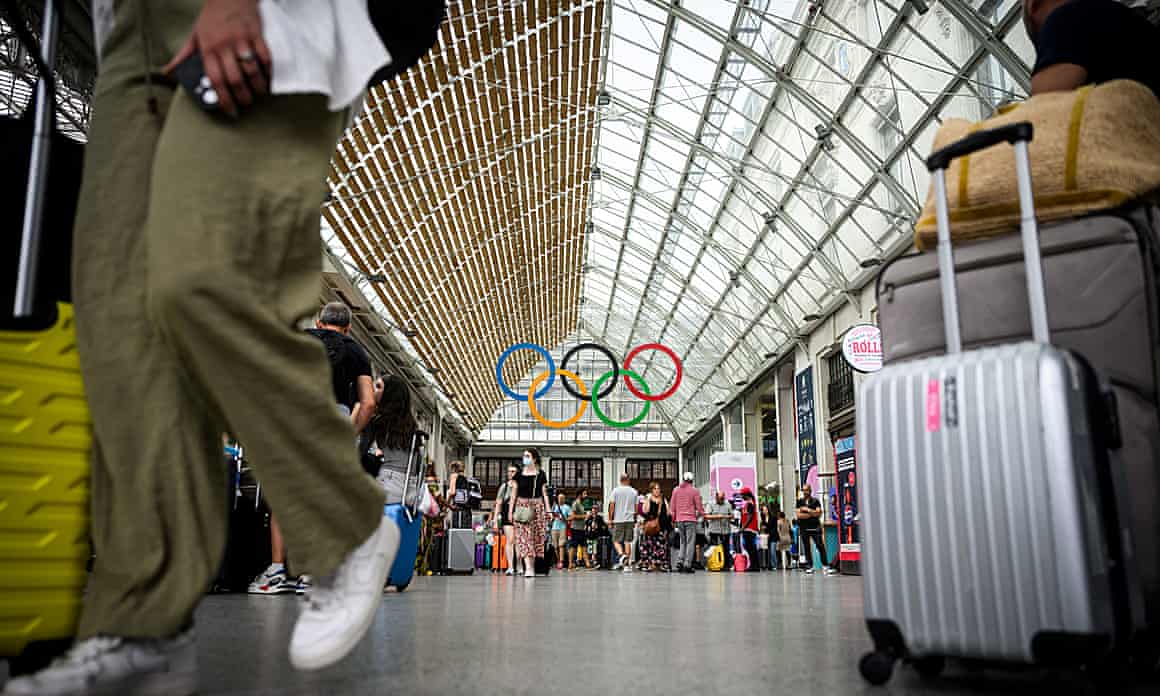 Travellers with rolling suitcases walk under the Olympic rings at the Gare de Lyon train station.