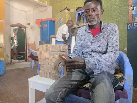 A seated Somali man counting banknotes while behind him another Somali man is at the door of a safe