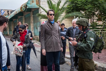 A soldier checks a festival participant’s ID while a group waits on a street