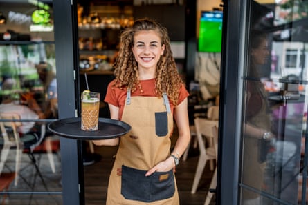 Smiling waitress wearing orange T-shirt and light orange apron serving a drink on a tray in a modern cafe