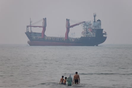 A vessel in the distance as a group of people paddle in the sea in the foreground