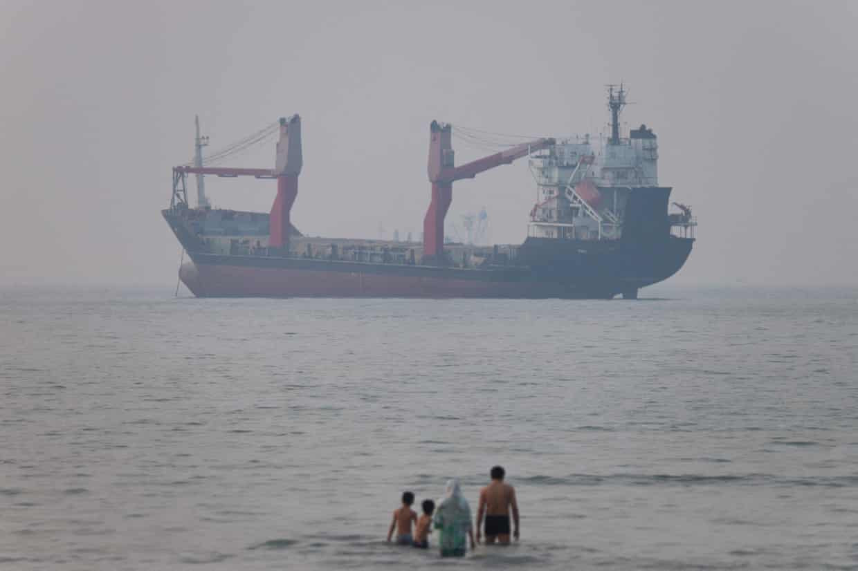 A vessel in the distance as a group of people paddle in the sea in the foreground