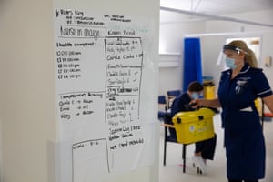 The staff schedule inside the vaccine distribution room as a nurse carries a box of used needles.