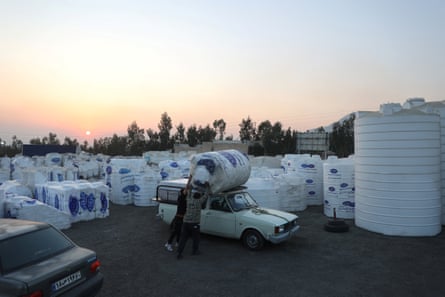 Men pushing a huge water tank on to the roof of a car to carry it home