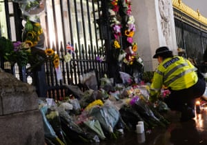 A police officer arranging floral tributes left outside Buckingham Palace in London