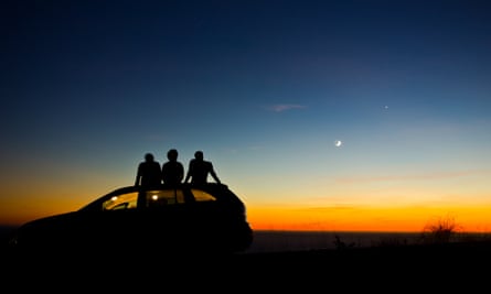 Three people watching the sun set from a car roof