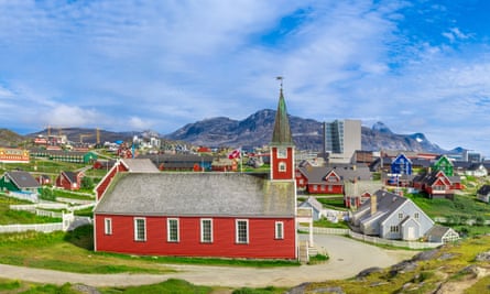 A red church in the foreground with other buildings and mountains in the background