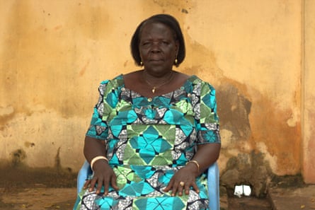 An older African woman in a bright dress poses solemnly in a seat