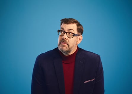 Richard Osman wearing a navy jacket and dark red polo neck