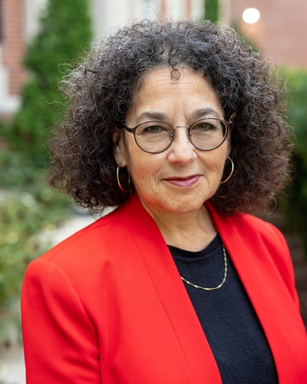 A woman with curly hair wearing a red blazer and black glasses.