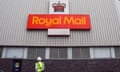 A man in a hi-vis jacket looks up at a Royal Mail logo and insignia on a warehouse