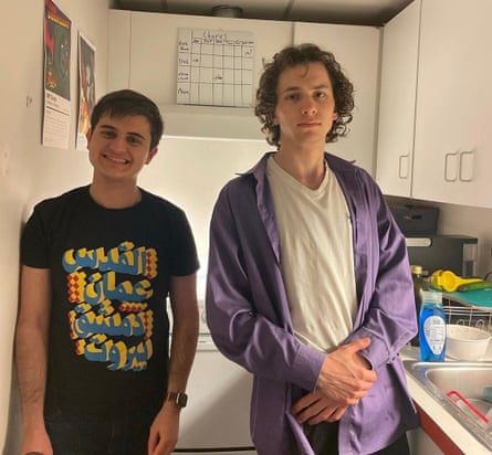 Two young men, one a head taller than the other, stand happily and awkwardly in a narrow kitchen.