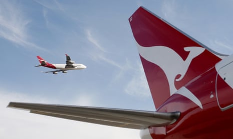 A Qantas 767 passenger jet flies over Sydney Airport in Sydney, Australia, while another plane sits on the tarmac