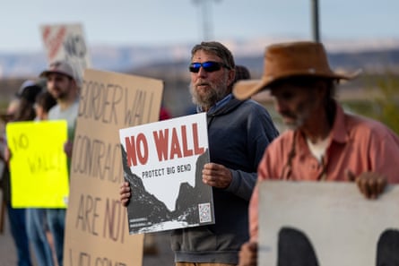 People stand in a line holding signs protesting against the construction of a border wall.