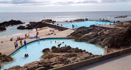 Two pools are carved into a rocky shoreline with curved and shaped edges to match the contours of the beach, with the sea behind.