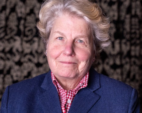 Sandi Toksvig wears a navy blazer over a red gingham shirt, smiling slightly