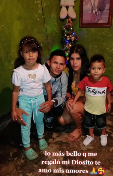 A man and a woman kneeling between two small children, a girl and a boy, in front of a small lighted Christmas tree.