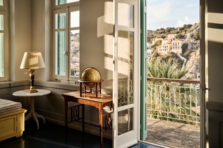 A hotel room with a door open on to a balcony and houses on a hillside beyond.