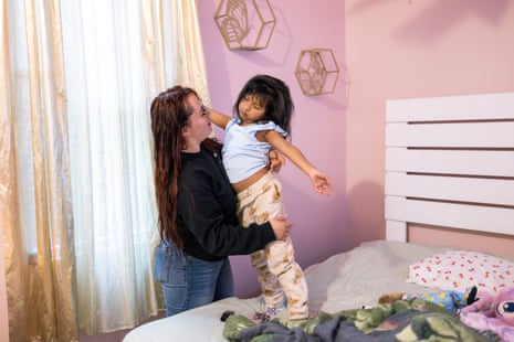A woman holds her daughter standing on a bed