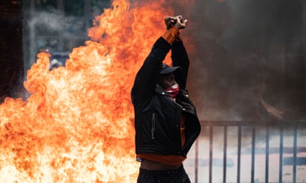 A man stands with his fists crossed over his head as a fire burns behind him