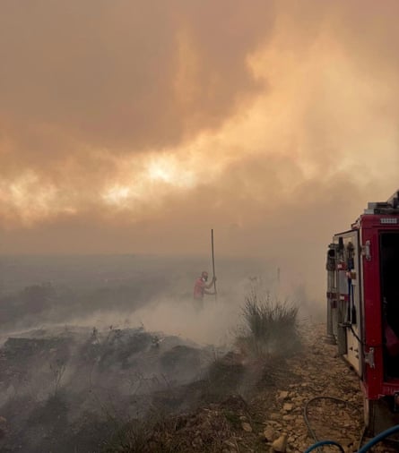 A firefighter works among thick smoke on moorland next to a fire engine