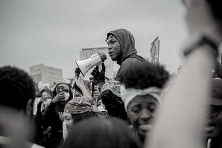 A young black man in a hooded sweatshirt speaks into a megaphone 