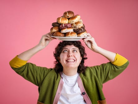 Lucy Knight smiling and balancing on her head a plate piled high with non-traditional hot cross buns