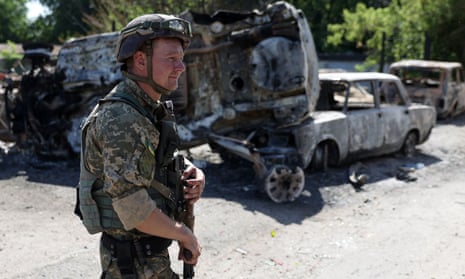 A Ukrainian serviceman walks past the wreckage of cars on a street in Lysychansk