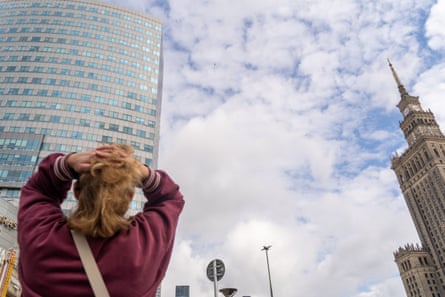 A woman holds her head while watching a man walk across a slackline between two high buildings.
