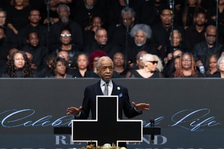a man in suit speaking with hands gestured at lectern marked with cross
