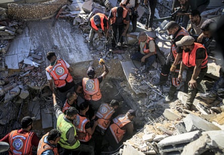 People in orange hi-vis vests try to dig through the wreckage of the building