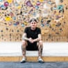 A man in a black T-shirt sitting in front of a bouldering wall.