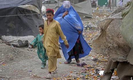A woman wearing a burqa and her children walk in front of their house in Kabul, Afghanistan