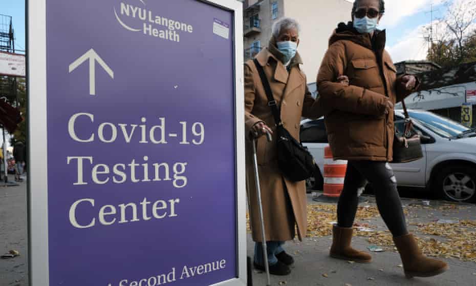 Two women in masks walk by a sign outside a New York City hospital that points the way to Covid testing facilities.